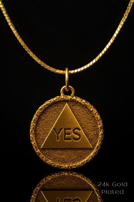 A 24k gold-plated pendant necklace with a triangular medallion featuring the word "YES" in the center.